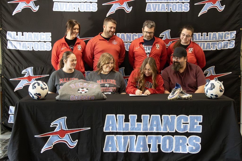 Ava signing her commitment letter with her coaches and family watching