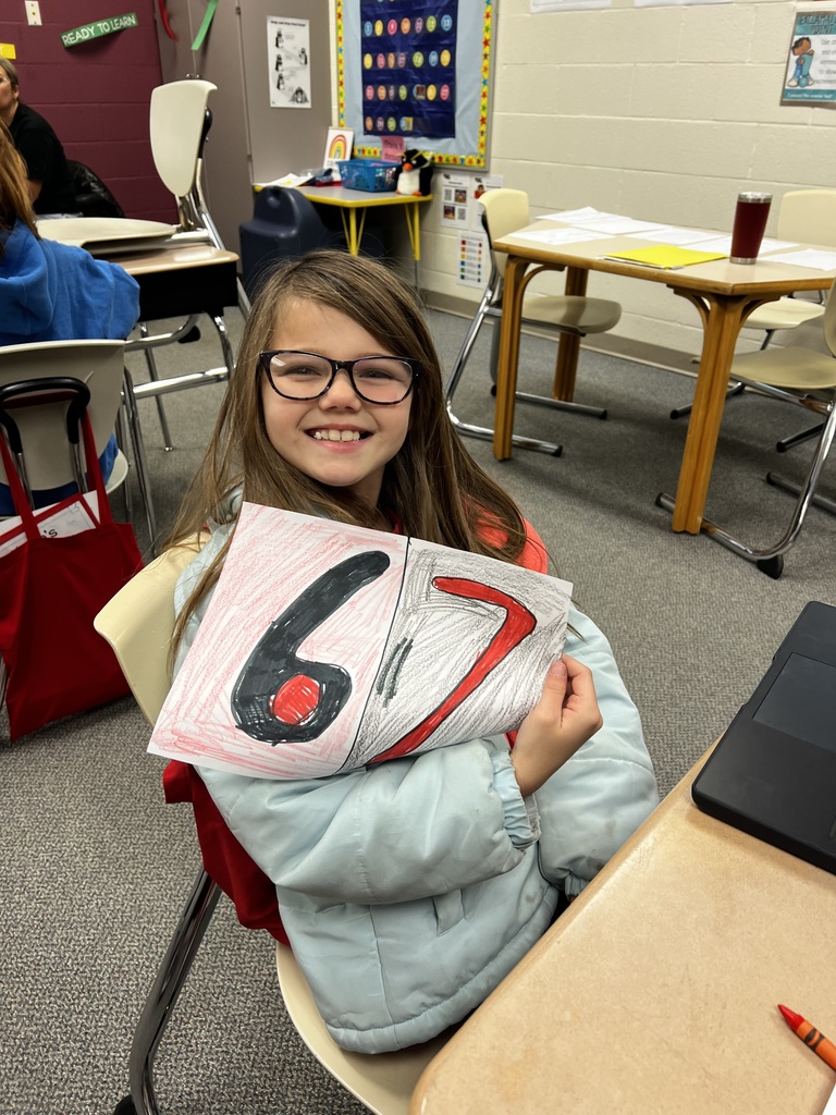 student holding up 6-7 that she drew and colored