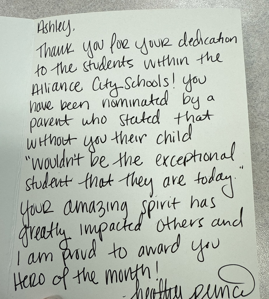 A handwritten note addressed to Ashley thanks her for her dedication to students in Alliance City Schools. The message shares that a parent nominated her, saying their child would not be the exceptional student they are today without her. The note praises her positive impact and awards her Hero of the Month.