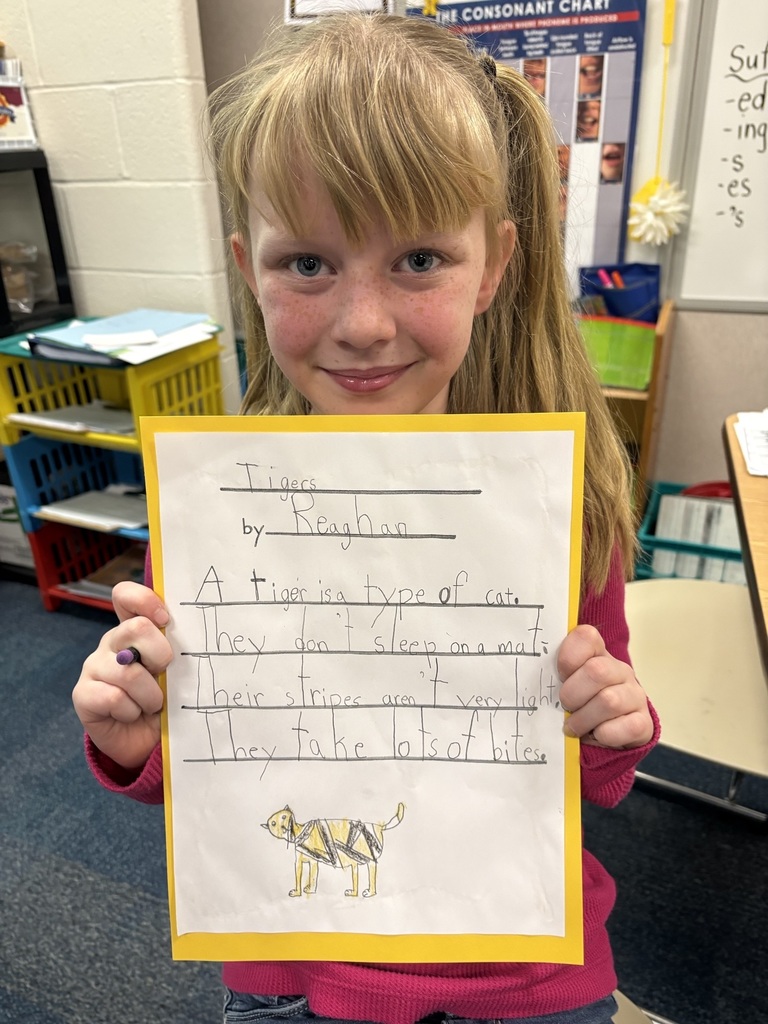 A student holding her poem about tigers: "A tiger is a type of cat. They don't sleep on a mat. Their stripes aren't very light They take lots of bites."