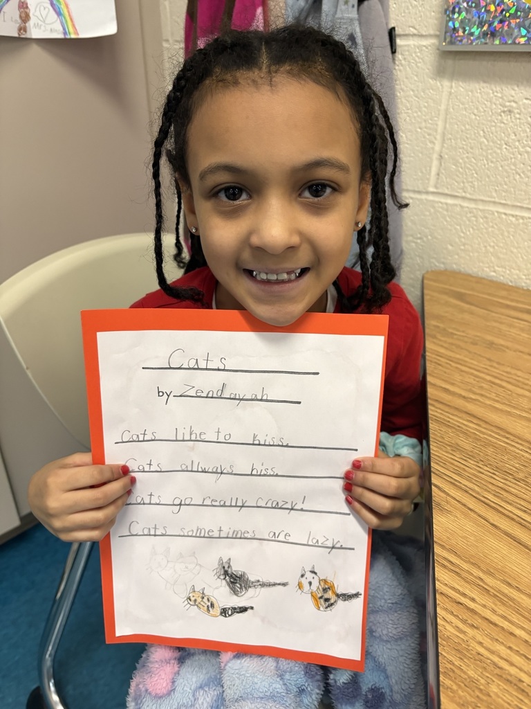 Student holding her poem about cats:  "Cats like to kiss. Cats always hiss. Cats go really crazy! Cats sometime are lazy."