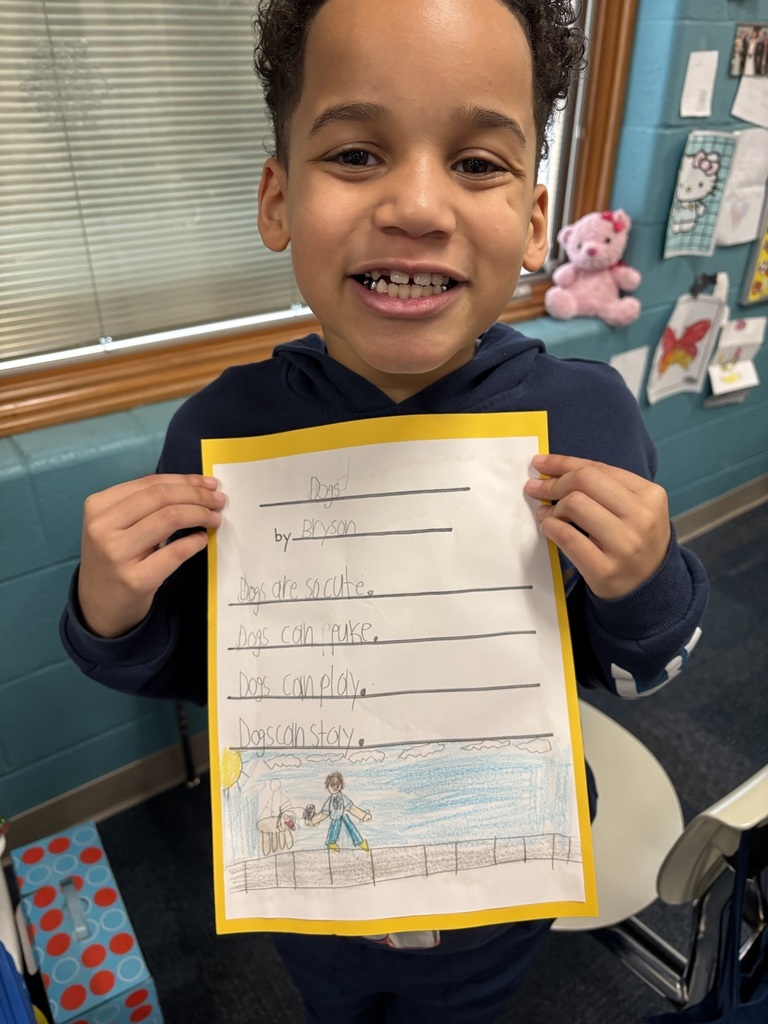 A student holding his poem about dogs: "Dogs are so cute. Dogs can puke. Dogs can play. Dogs can stay."