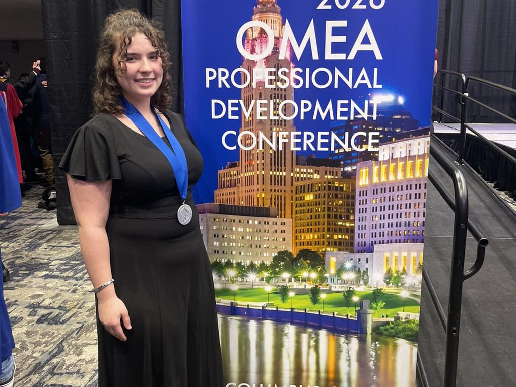 Makenna standing by a sign for the OMEA conference
