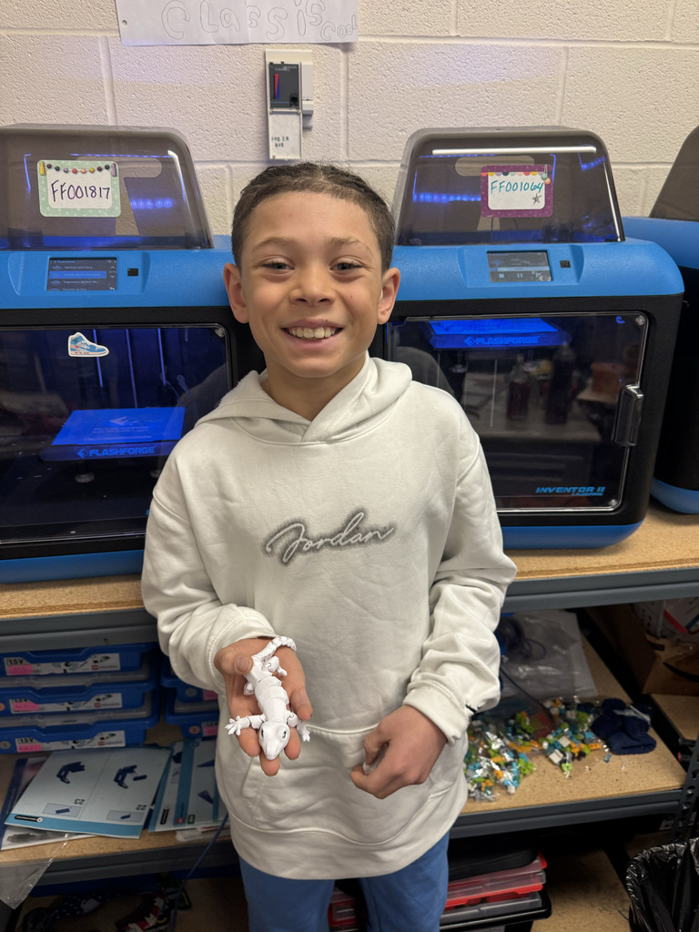 Ja'Cobi standing in front of the printers holding a 3D-Printed gecko he made