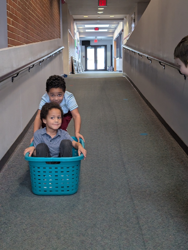 A student sitting in a basket and another student pushing it like a bobsled