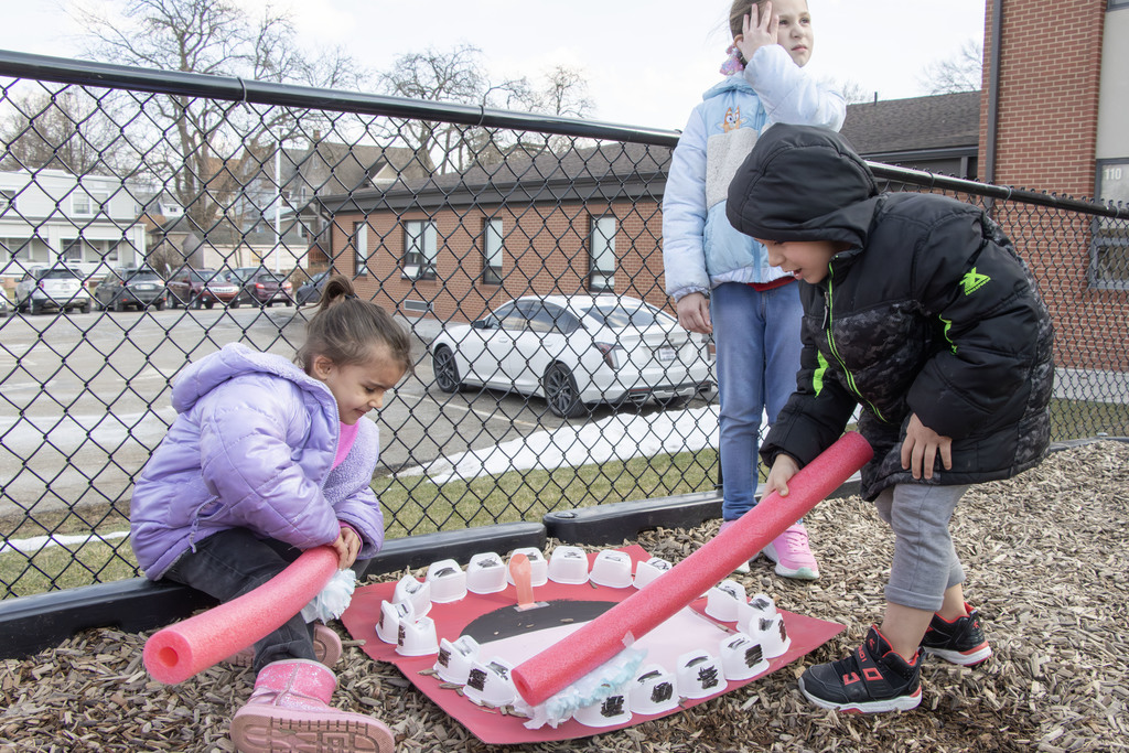 Students using pool noodles with swiffer cloths on them to mimic toothbrushes cleaning off pringle cups that have been taped to paper to look like a mouth with teeth. The teeth have marker on them that gets cleaned off with the toothbrushes.