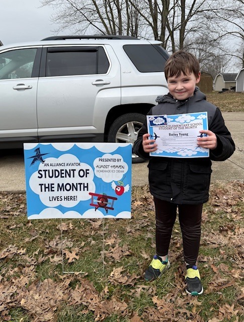 A student holding his certificate and standing by his yard sign