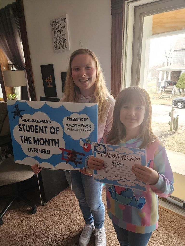 a student holds her certificate while her teacher hold a yard sign