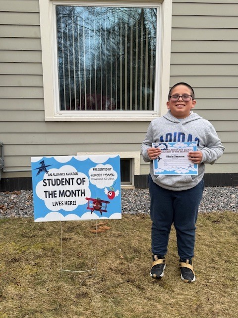 A student holding his certificate and standing by his yard sign