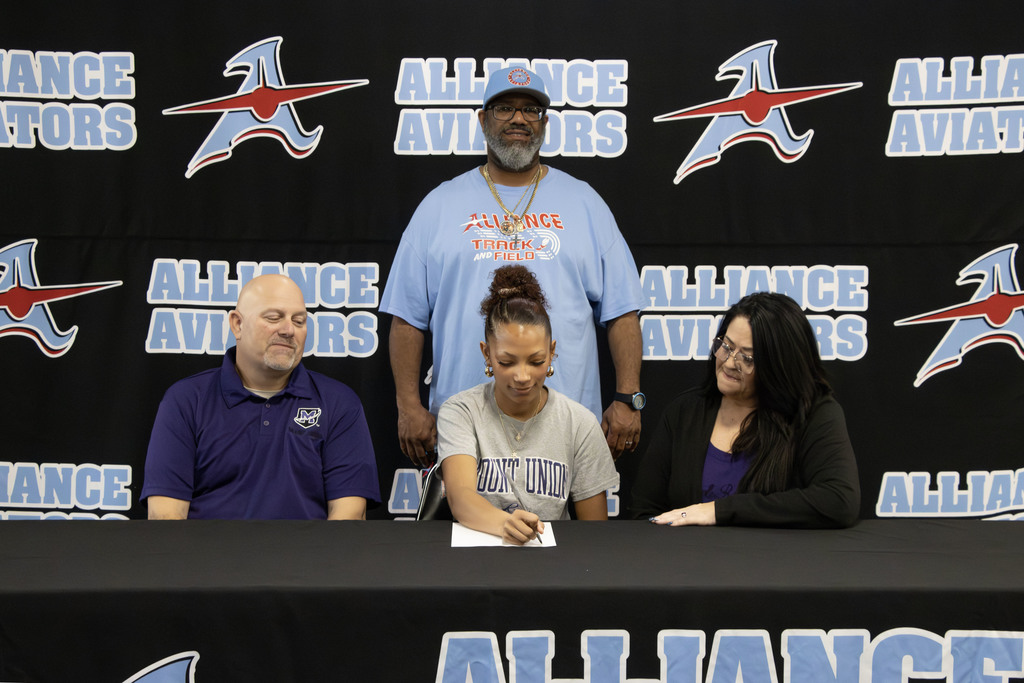 Kyliana signing a pice of paper while her coach Korey Stevens and her parents watch