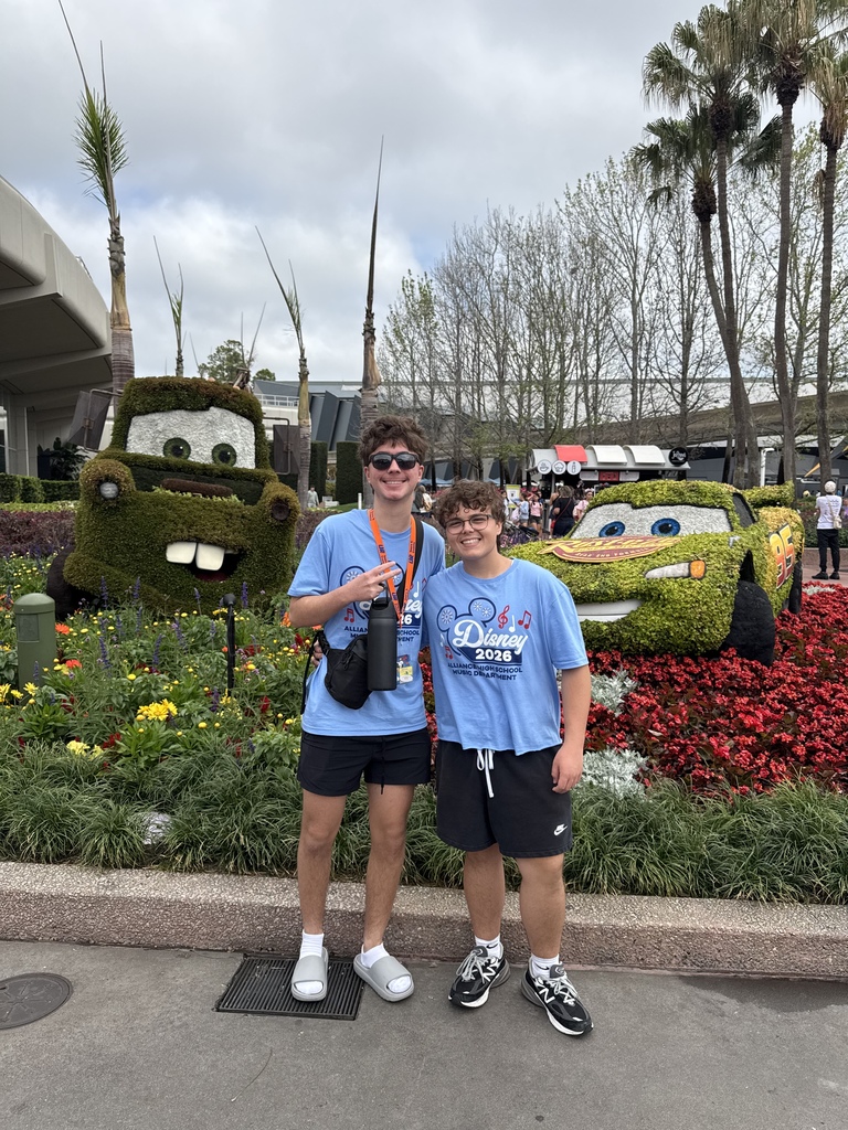 Two students standing infront of shrub shaped like characters from Cars