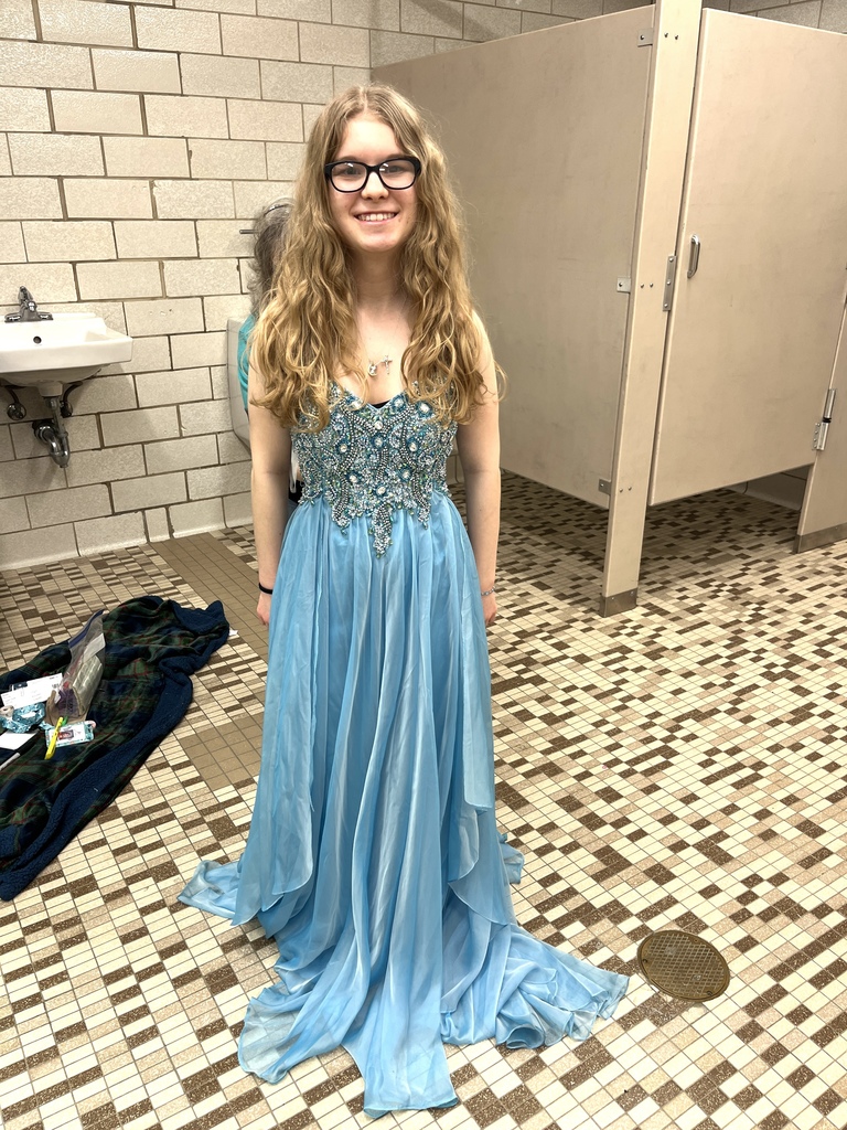 A student smiles while trying on a light blue dress with gemstones on top