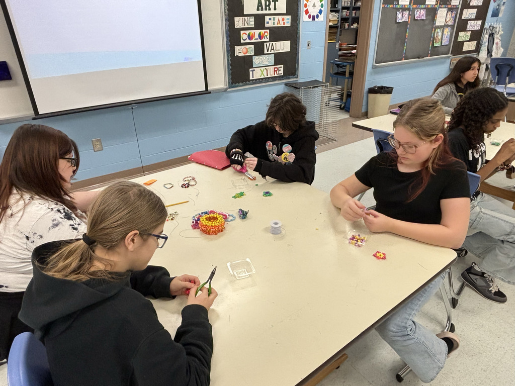 4 sitting at a table making crafts out of beads and wire