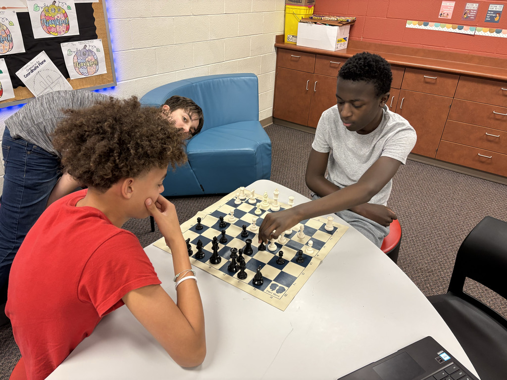 Two students playing chess while a third watches