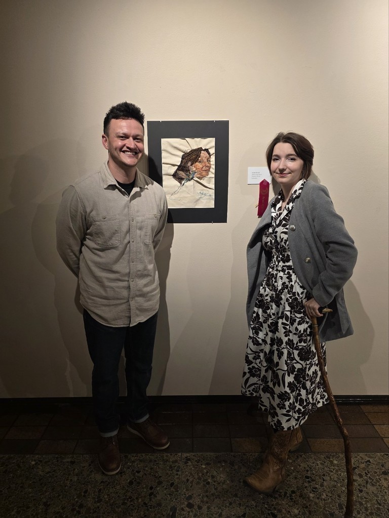 Audrey and her high school art teacher, Steve Cabassa, standing next to her art work hanging on a wall