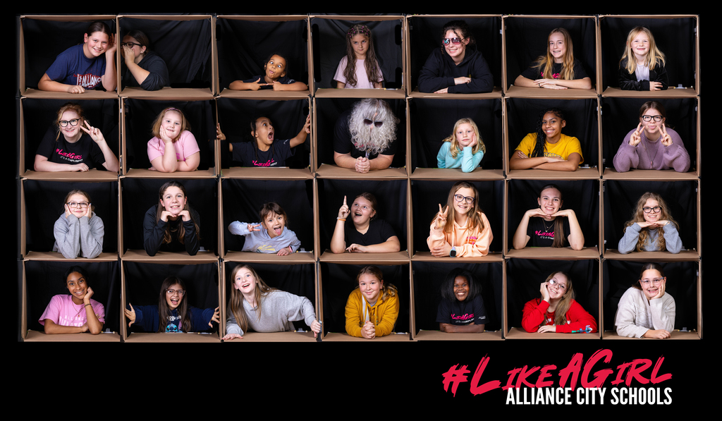 A collage of students arranged in a grid of open box frames, each student posing with different expressions and gestures. The group includes a diverse mix of girls smiling, laughing, making peace signs, and showing playful personalities. One box includes a person wearing a fun costume with a white wig and sunglasses. The background is black, making the cardboard box frames stand out. Text in the bottom corner reads “#LikeAGirl Alliance City Schools.”