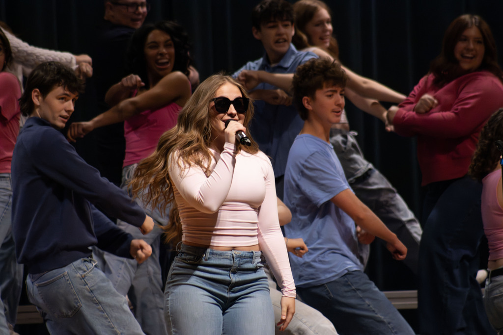 a student sings animatedly with sunglasses on while others dance in the background