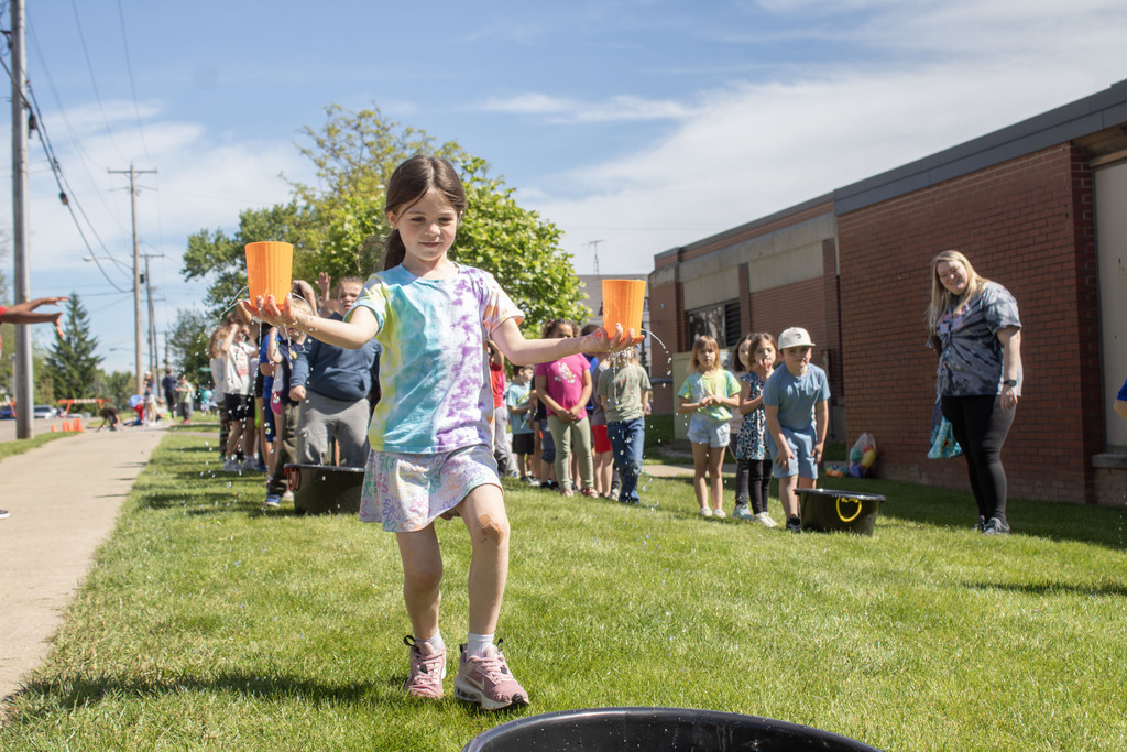 student running towards a bucket while holding two cups with water