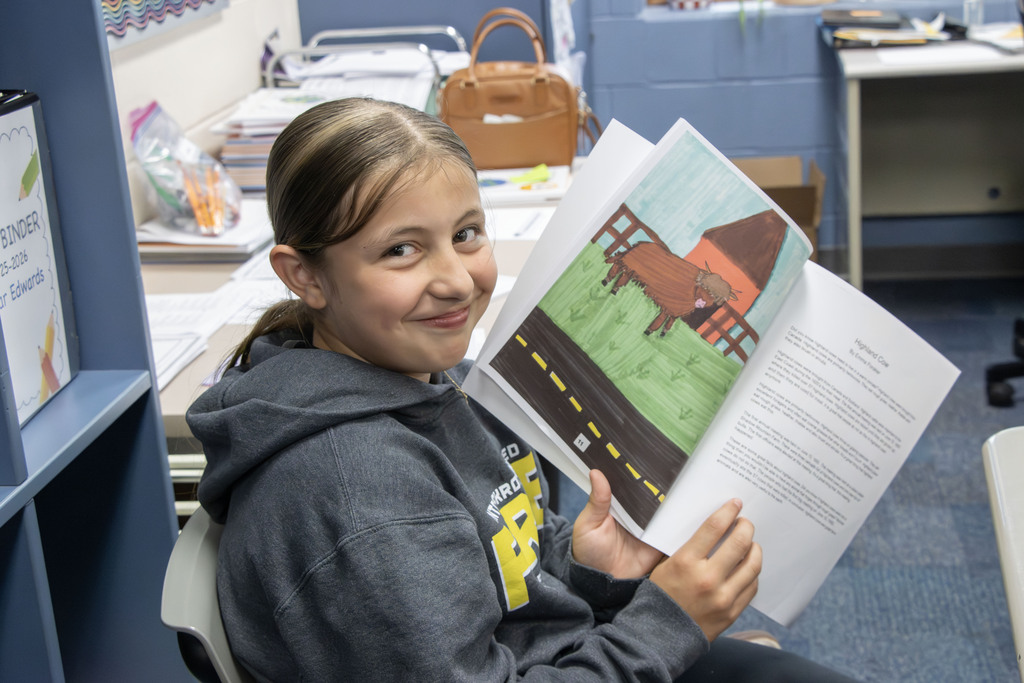 A student holding up the pages she wrote and illustrated