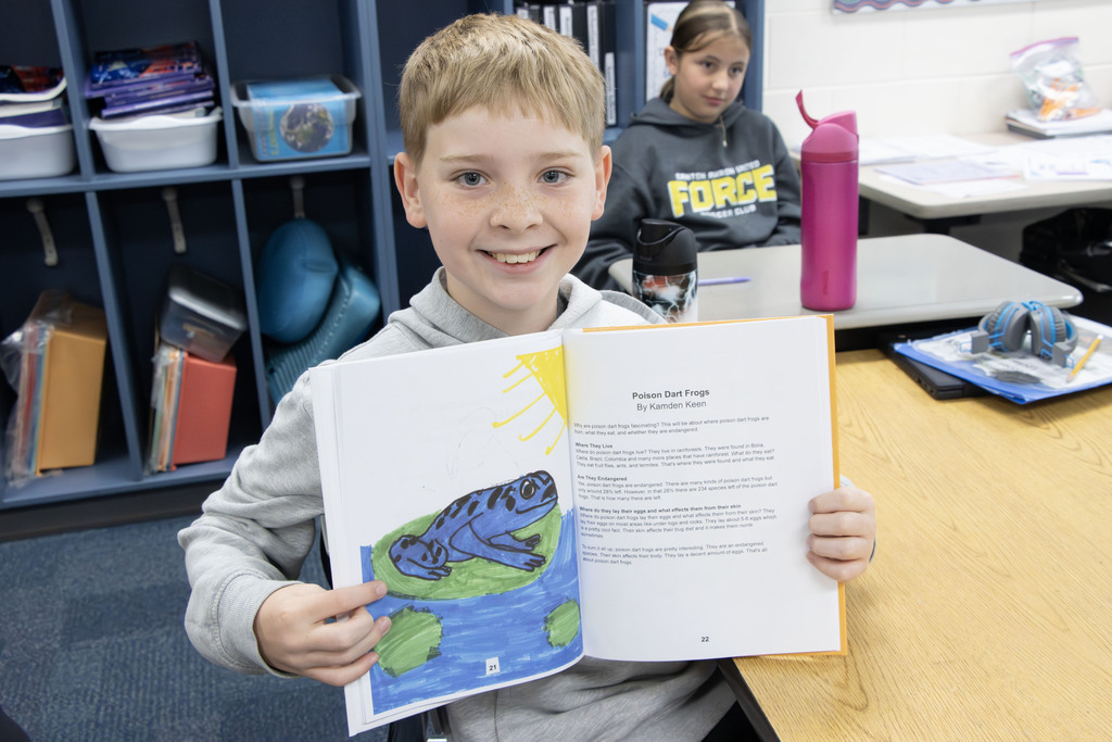 A student holding up the pages she wrote and illustrated