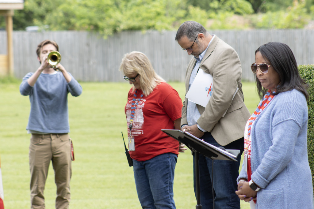 A student plays taps on the trumpet while people bow their heads