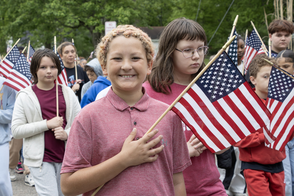 A student holds an America flag over his heart while smiling