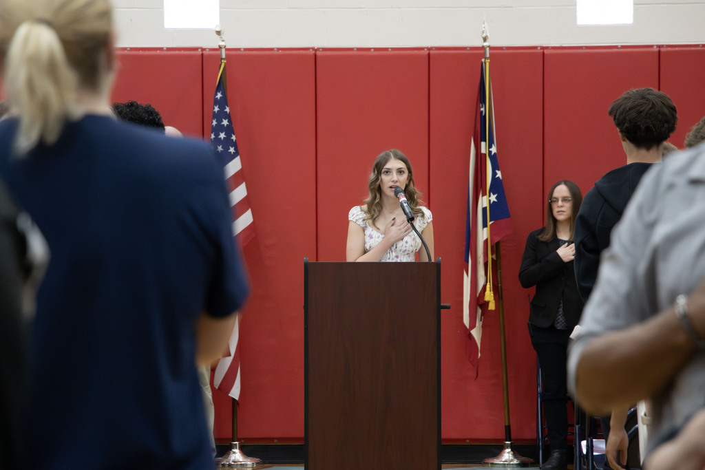 student saying the pledge of allegiance while people stand.