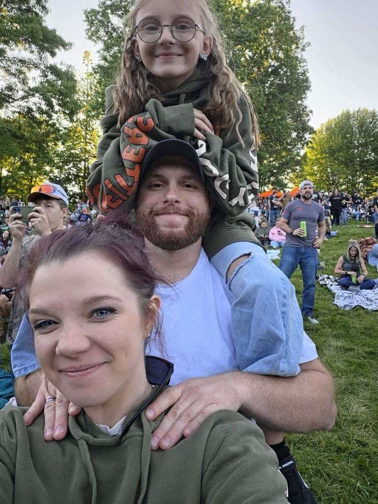 Joei flaker on her fathers shoulders while her mom stands in front of the two smiling.