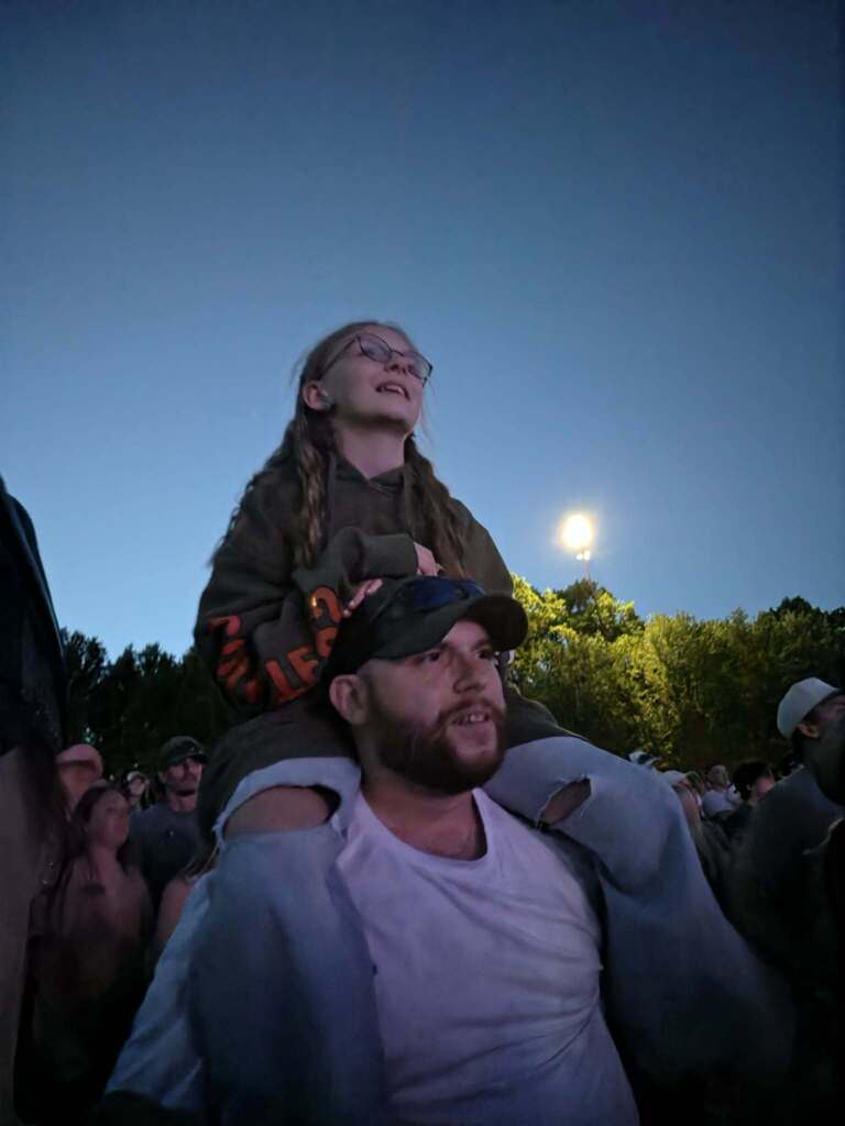 Joei flaker on her fathers shoulders while she watches the concert at dusk