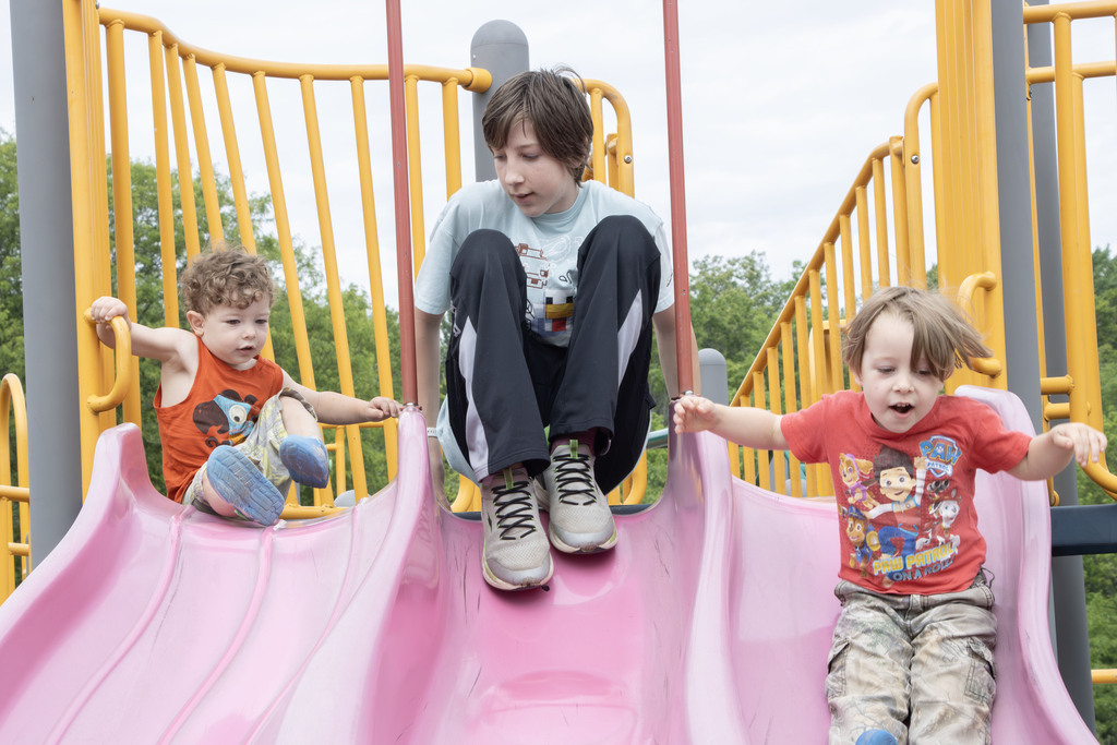 two young students and an older sibling slide down the slides