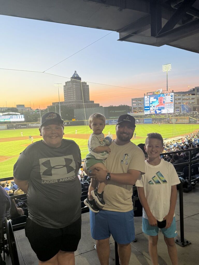 Barret and Andrew standing next to Mr. Kimble with the baseball game in the background