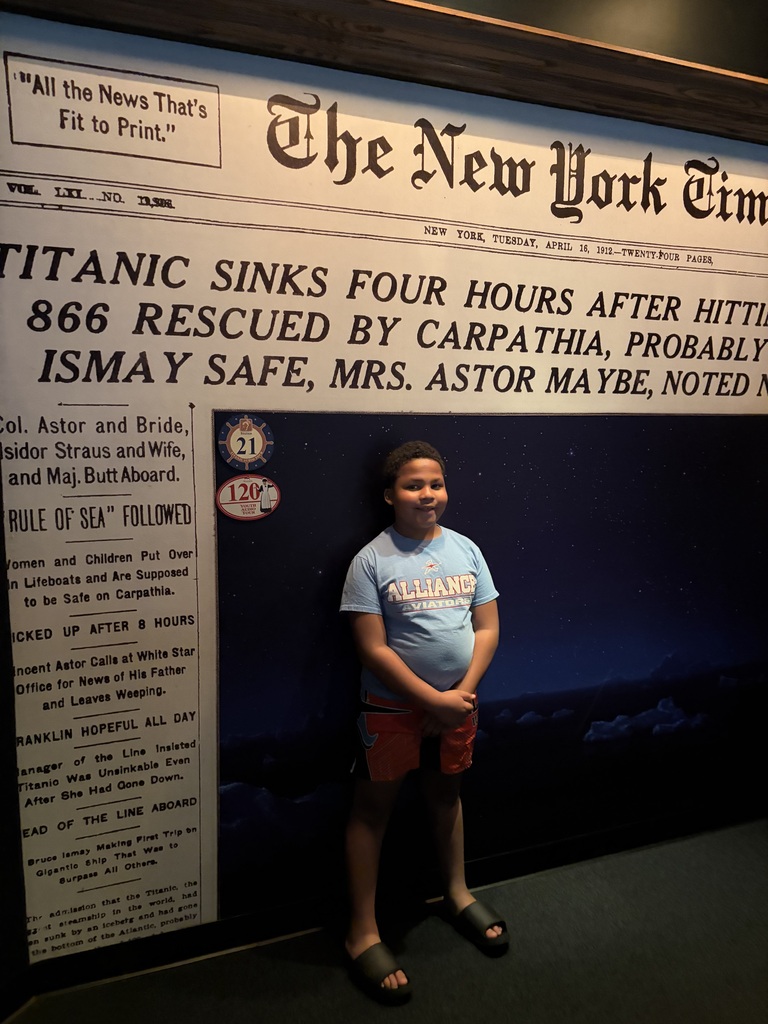 Russell standing in front of a wall painted to look like the headline page of the newspaper that announced the titanic