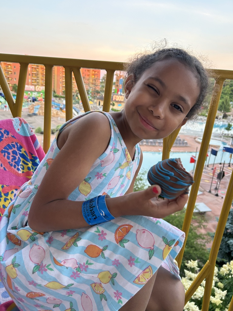 Kynslee smiling while eating a cookie on the balcony with a pool in the background