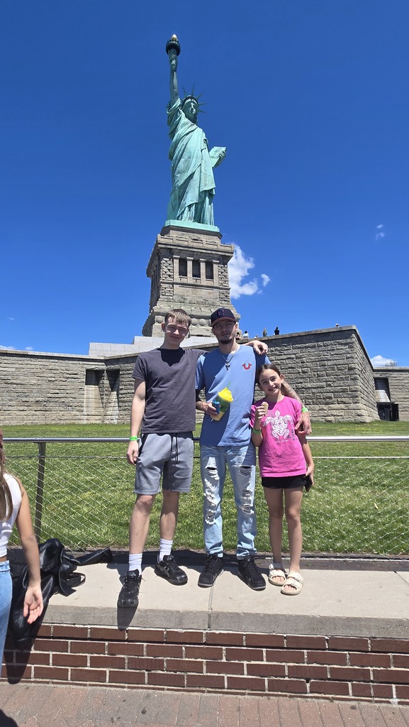Adelyn, Kevin and their parent pose for a picture in front of the statue of liberty