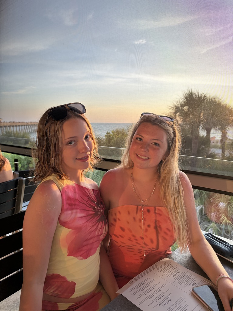 Aylamae and Catey sitting at a table overlooking the water at sunset