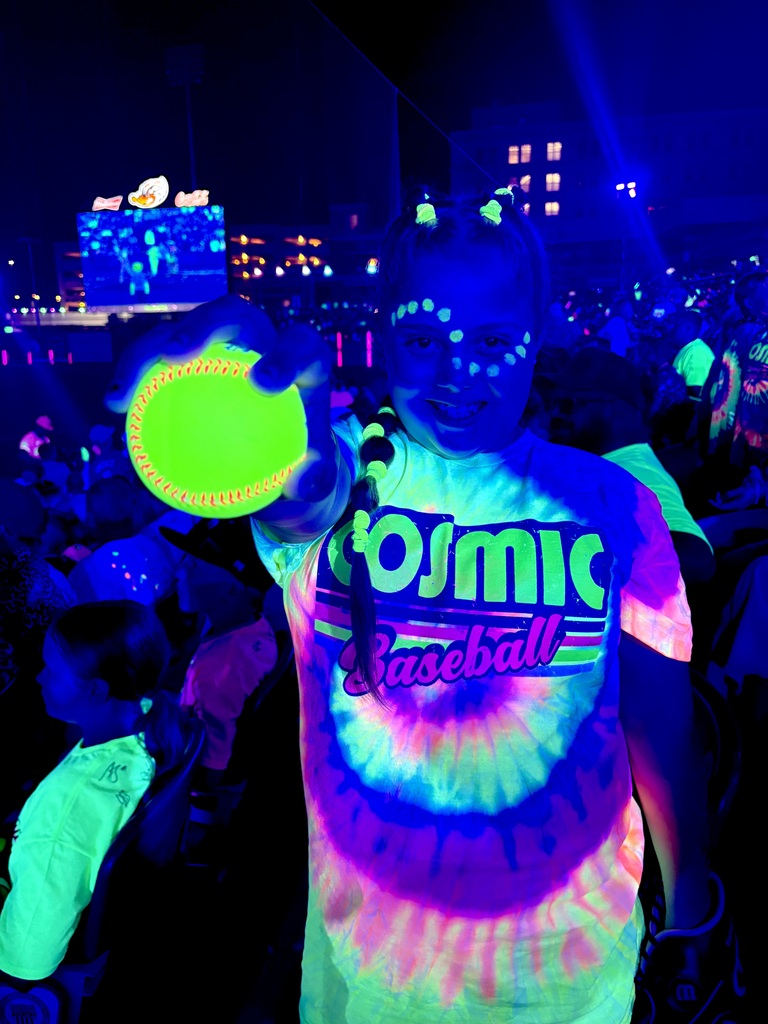 Hannah holding a baseball while wearing a tie dye shirt and neon paint at the cosmic baseball game