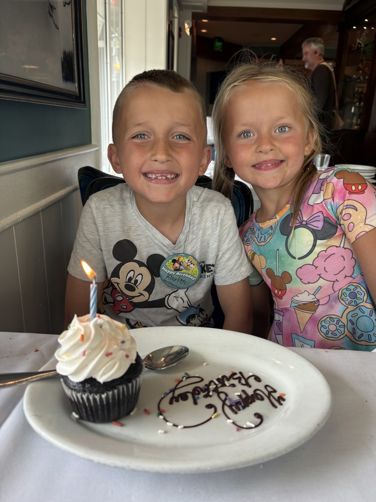 Kalyton and Emajean smiling with a plate saying "Happy Birthday" and a chocolate cupcake with a candle in it in front of them