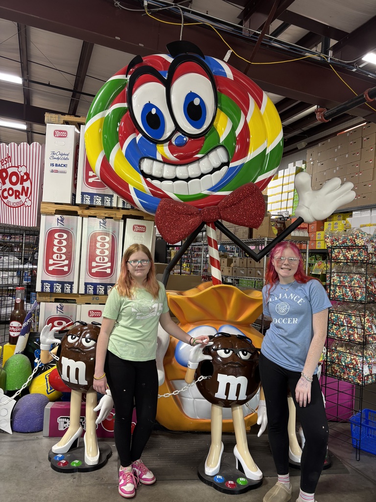 The students standing in front of a giant lollipop with eyes and a mouth