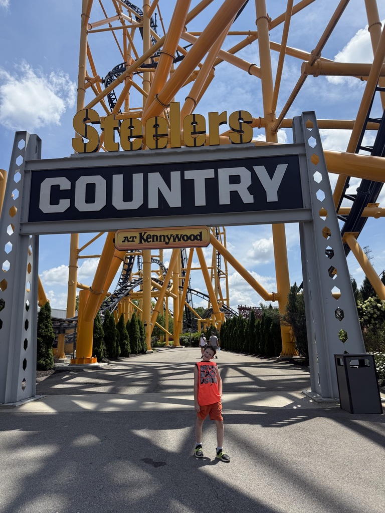 Timothy standing in front of a roller coaster and a sign that says Steelers County at Kennywood
