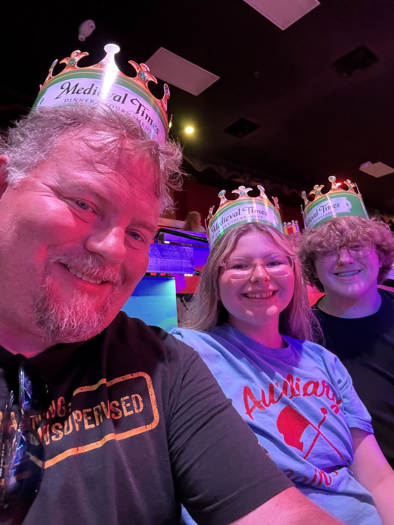 Ava smiling for a picture with her dad and brother while wearing paper crowns