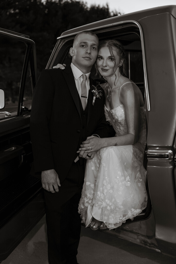 A black and white photo of Haley and her husband on their wedding day sitting in a truck