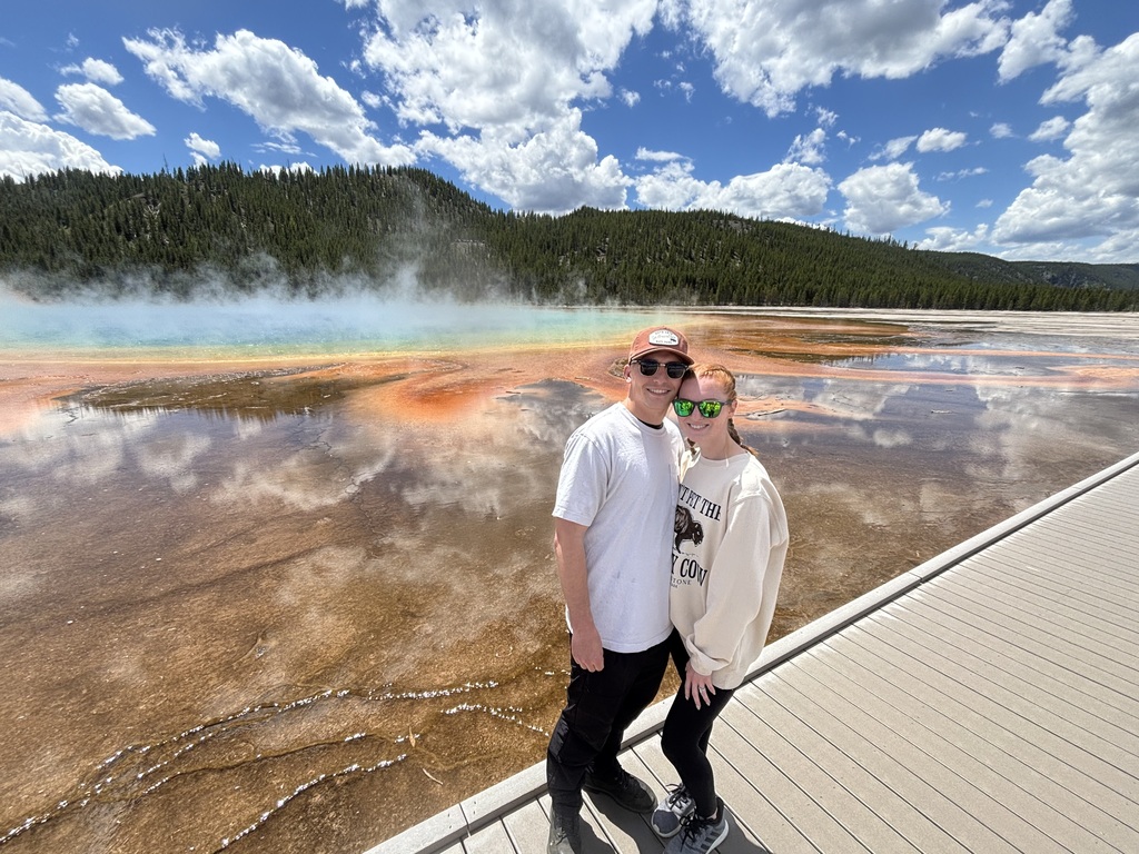 Haley and her husband standing in front of the Grand Prismatic Springs