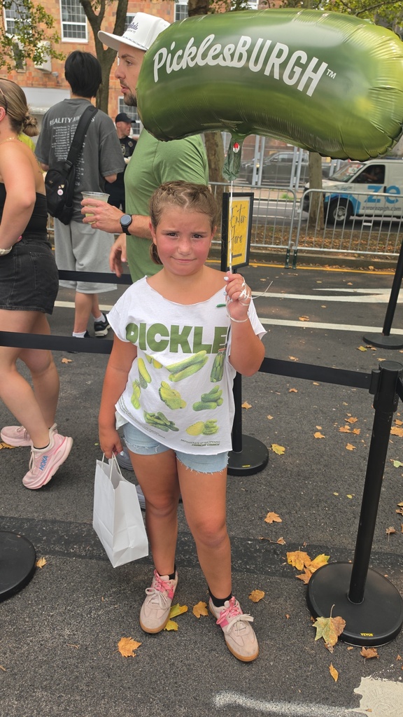 Kasidi posing for a picture wearing a shirt with pickles on it and a balloon that says Picklesburgh
