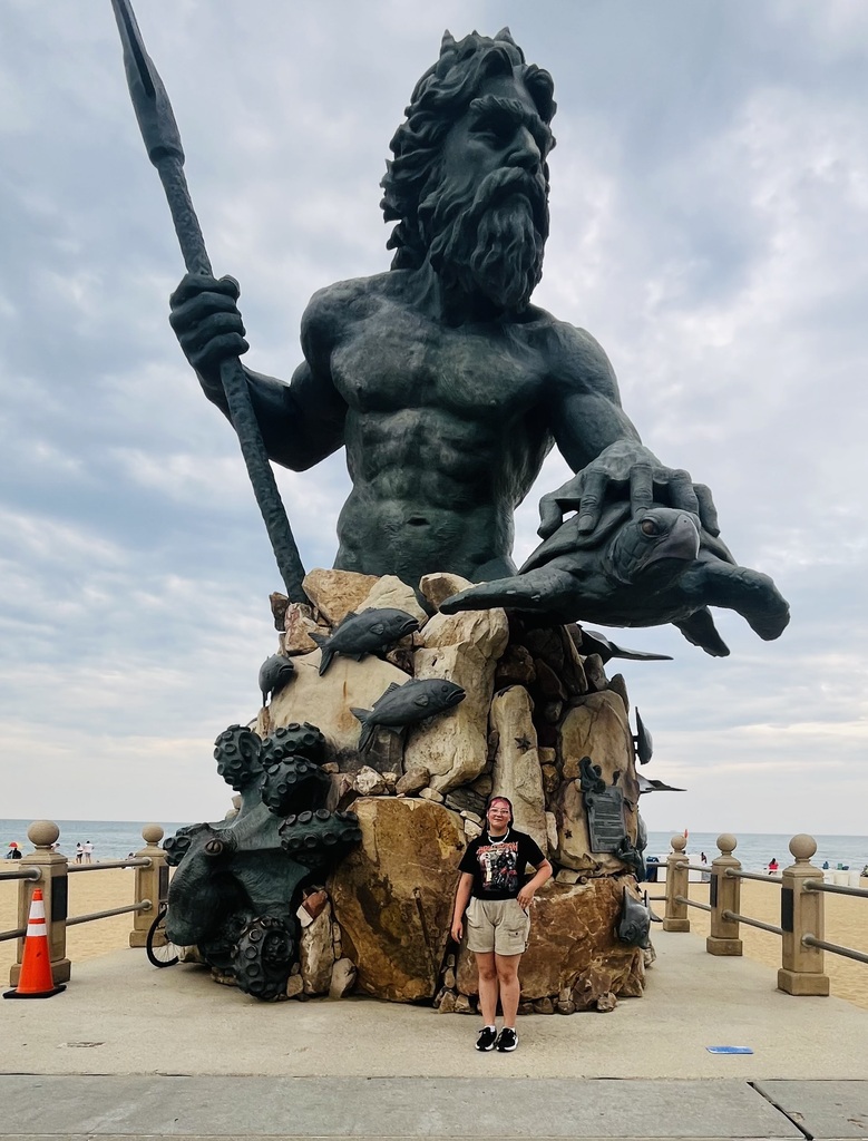 Harleigh standing next to a guant statue of Poseidon on the beach