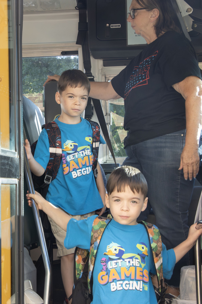 Two twin boys dressed a like exit a school bus while the bus driver watches the students