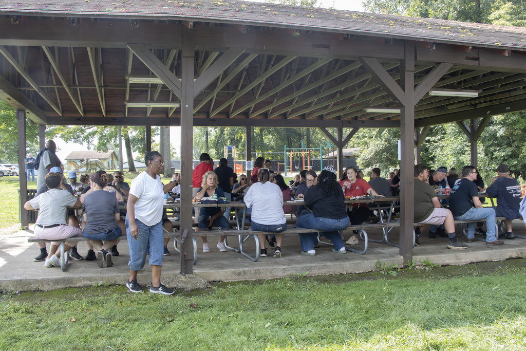 a large group of staff members eating pizza at picnic tables