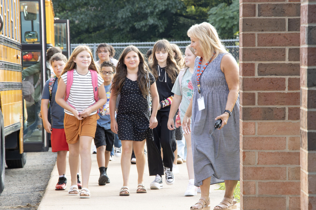 A staff member walking in front of a group of staff members while they smile.
