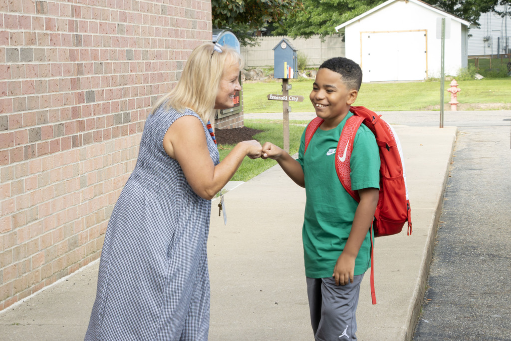 A staff member in a dress giving a fist bump to a student wearing a red backpack