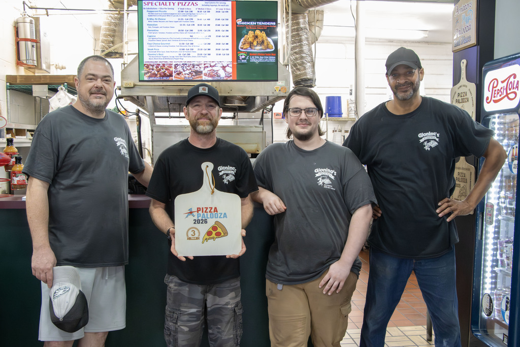 Picture of 4 gioninos staff members with the middle one holding a pizza peel decorated as the award