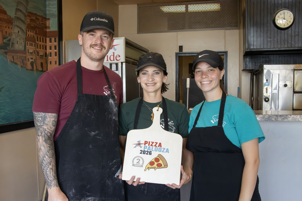 Three pizza shop employees pose for a picture while holding a decorated pizza peel as the award